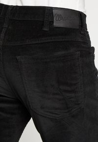 Zwarte corduroy broek met een gestructureerd oppervlak, voorzien van een leren taillebandlabel en een achterzak met stiksels.