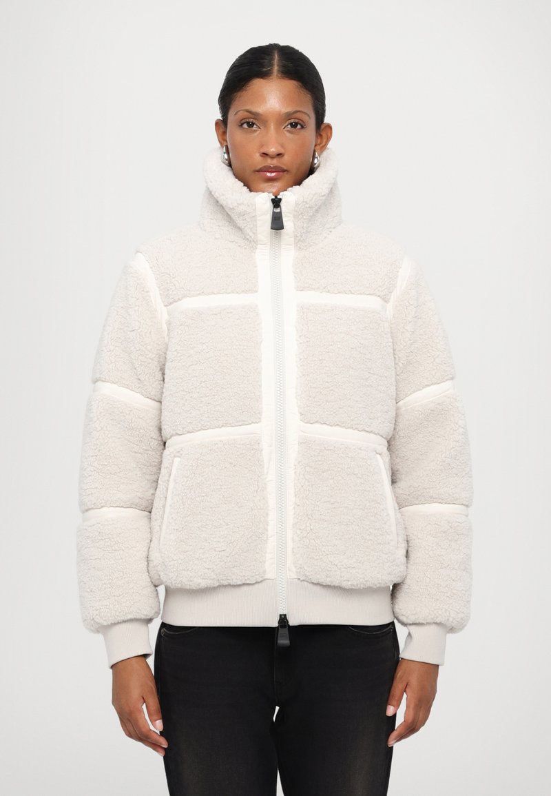 Kermitehtävä fleece-takki, jossa on korkea kaulus, vetoketjukiinnitys ja vaakasuuntainen raidallinen muotoilu. Varustettu etutaskuilla ja ribbaamalla hihansuilla.