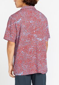 Camisa de manga corta con un fondo azul y un patrón abstracto en forma de coral rojo, hecha de una tela ligera, con un corte holgado y cuello.
