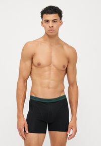 Boxeri negri cu un brâu elastic branduit de culoare verde. Textură de țesătură netedă și design aderent. Fără modele sau accente vizibile.