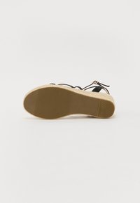 Musthave musta espadrille platvormsandaal looduslike jute keskmise talla, kummist välispinna ja reguleeritava pahkluu rihmaga. Tekstureeritud tald haarde saavutamiseks.