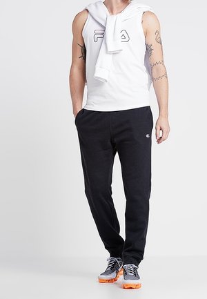 Vit ärmlös tröja med en logotyp, mörkblå mjukisbyxor och sportiga sneakers med orange sulor. Outfiten har en huva på toppen som är hängd över axlarna.