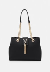 Svart handväska med guldiga kedjeremmar, en platt framsida och en tofsdetalj. Har en framträdande logotyp i mitten och en texturerad yta.