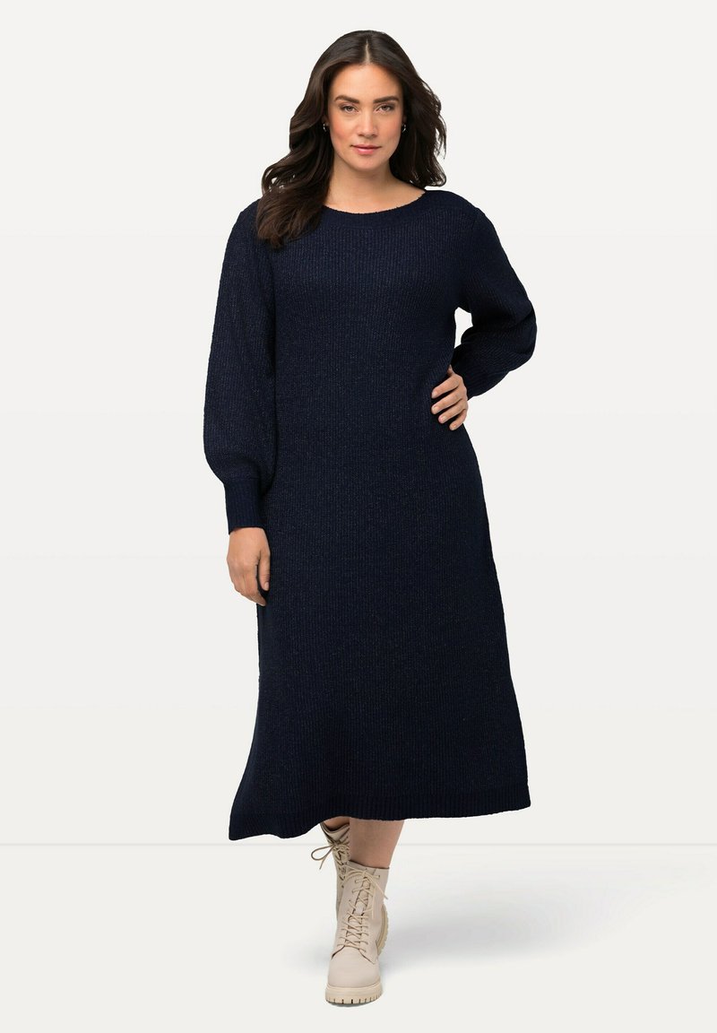 Robe en tricot bleu marine à coupe décontractée, avec des manches longues, un col rond et un tissu texturé. Associée à des bottines beige clair à lacets.