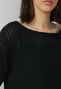 Zwarte gebreide trui met een losse, open weefpatroon. Heeft een ruime halslijn en ribbelrandjes. Gestructureerd oppervlak met verticale strepen.