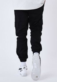 Pantaloni cargo neri con polsini elasticizzati, con tasche laterali, abbinati a sneaker bianche Nike e con dettagli a coste alla caviglia.