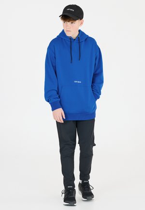 Blå hoodie med framficka och svarta dragband, tillsammans med svarta slim fit-byxor och svarta sneakers, med en logotyp på båda plaggen.