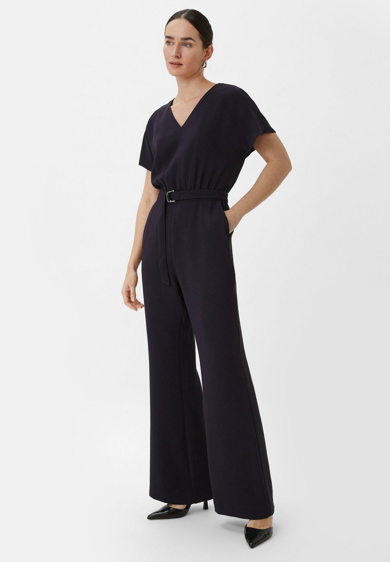 Marineblauer Jumpsuit mit V-Ausschnitt, kurzen Ärmeln, tailliertem Gürtel, weit geschnittenen Hosenbeinen und seitlichen Taschen, kombiniert mit schwarzen, spitz zulaufenden High Heels.