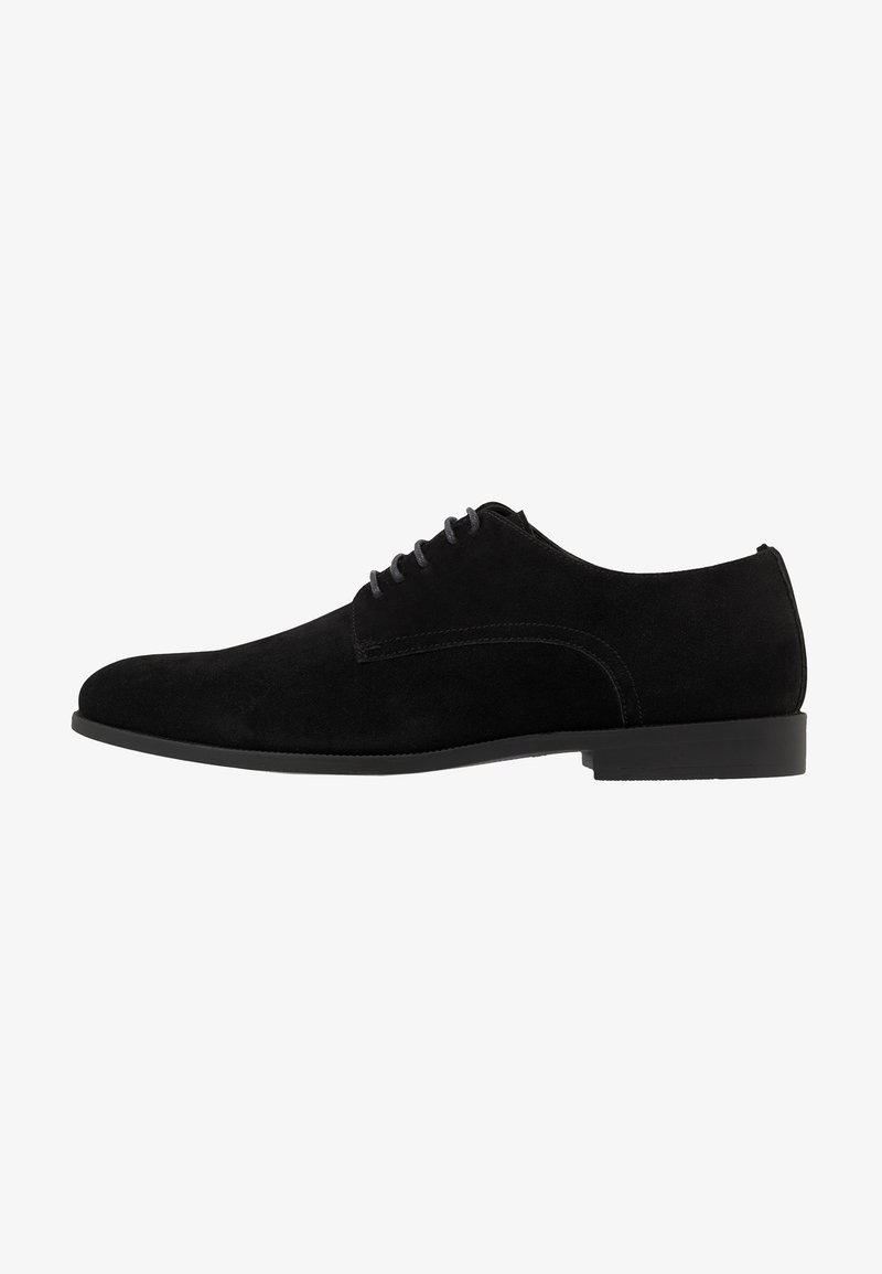 Chaussure habillée pour homme en suede noir à lacets, avec un talon bas et un design épuré et minimaliste, présentée de côté sur un fond blanc.