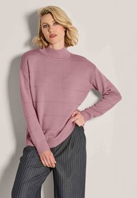 Gestrickter Pullover in sanftem Pink mit hohem Kragen und gerippten Bündchen. Verfügt über horizontale Strukturlinien und einen lässigen Schnitt. Kombiniert mit gestreiften Hosen.