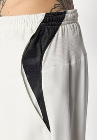 Hvite treningsshorts med en svart meshpanel på siden. Elastisk midjebånd med en jevn tekstur og sømdetaljer.