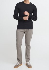 Pullover blu navy a maglia con un motivo testurizzato, colletto rotondo, abbinato a chinos grigio chiaro e sneakers grigie con strisce bianche.