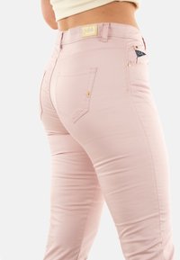 Jeans ajustados de color rosa claro, hechos de una tela elástica, con una cintura alta, bolsillos traseros y detalles en tono dorado.