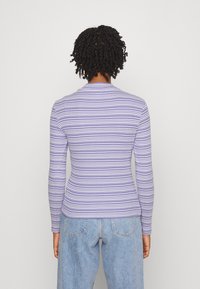 Dlouhý rukáv, přiléhavý top s horizontálními pruhy v purpurové a bílé barvě, kulatým výstřihem a žebrovanou strukturou. Spárováno s džínami s vysokým pasem.