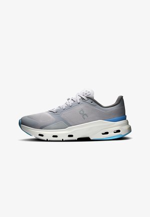 Zapatilla deportiva de color gris claro con suela blanca, detalles en azul, parte superior de malla, logo en el lateral y cordones, mostrada en perfil derecho sobre fondo blanco.