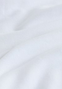 Fehér szövet sima, kissé texturált felülettel, finom redőkkel és gyűrődésekkel, amelyek egy könnyű anyagra jellemzőek.