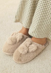 Syntetiske pels slippers i beige med en rund tå, prydet med kaninører og pom-pom detaljer foran. Blød tekstur, hyggeligt design.