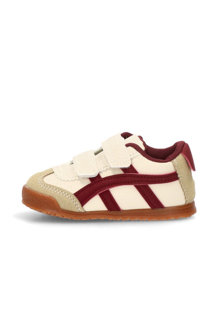 Zapatillas deportivas infantiles con una parte superior de color blanco crema, acentos burdeos y dos tiras de velcro. Presentan una suela de goma texturizada y franjas laterales en contraste.