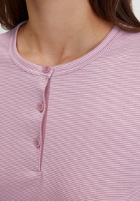 Top a righe rosa con scollo rotondo, tre piccoli bottoni sulla piastrella e una texture di tessuto morbido.