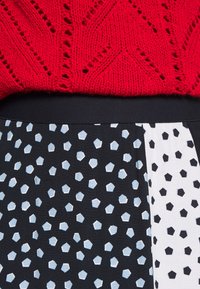 Suéter rojo de punto con un patrón texturizado sobre una falda negra con un estampado geométrico de hexágonos en azul claro y blanco.