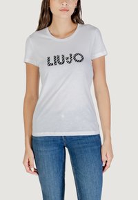 T-shirt bianco di cotone con il logo "LIU JO" in nero con un motivo testurizzato, maniche corte e scollatura rotonda, abbinato a jeans blu.