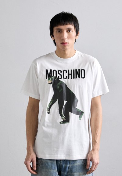 T-shirt bianca in cotone con una grande grafica di scimpanzé nera e verde e la scritta "MOSCHINO" in bold nero. Vestibilità casual e maniche corte.
