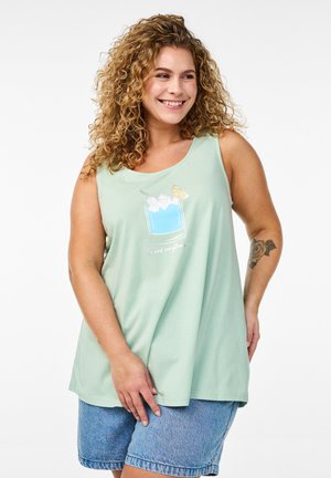 Top sin mangas de color verde claro con un gráfico de una bebida, hielo y una rodaja de limón. Textura suave, ajuste holgado, combinado con pantalones cortos de mezclilla.