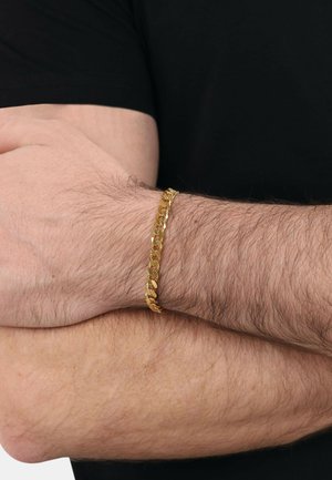 Goldene Kettenarmband mit ineinandergreifenden Gliedern, das eine polierte Oberfläche und eine glatte Textur aufweist, am Unterarm vor einem schwarzen Hintergrund getragen.