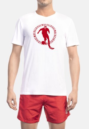 Witte katoenen T-shirt met een rood afbeelding van een speler en tekst, rond ontwerp met driekwart mouwen. Gecombineerd met rode korte broek.