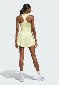 Keltainen urheilumekko, jossa on vartalonmyötäinen yläosa ja levenevä helma, varustettuna urheilullisella selkämyksellä. Mallilla on valkoiset sukat ja vaaleansiniset kengät.