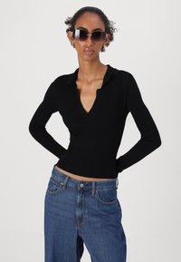 Haut noir à manches longues en côtes avec un col et un décolleté en V profond, associé à un jean en denim bleu taille haute avec des coutures visibles et des poches.