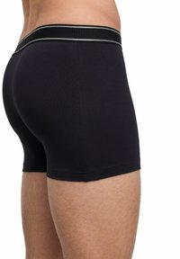 Black cotton boxer shorts with a fitted design. Features a soft, elastic waistband with a contrasting stripe. Smooth texture and tailored fit.