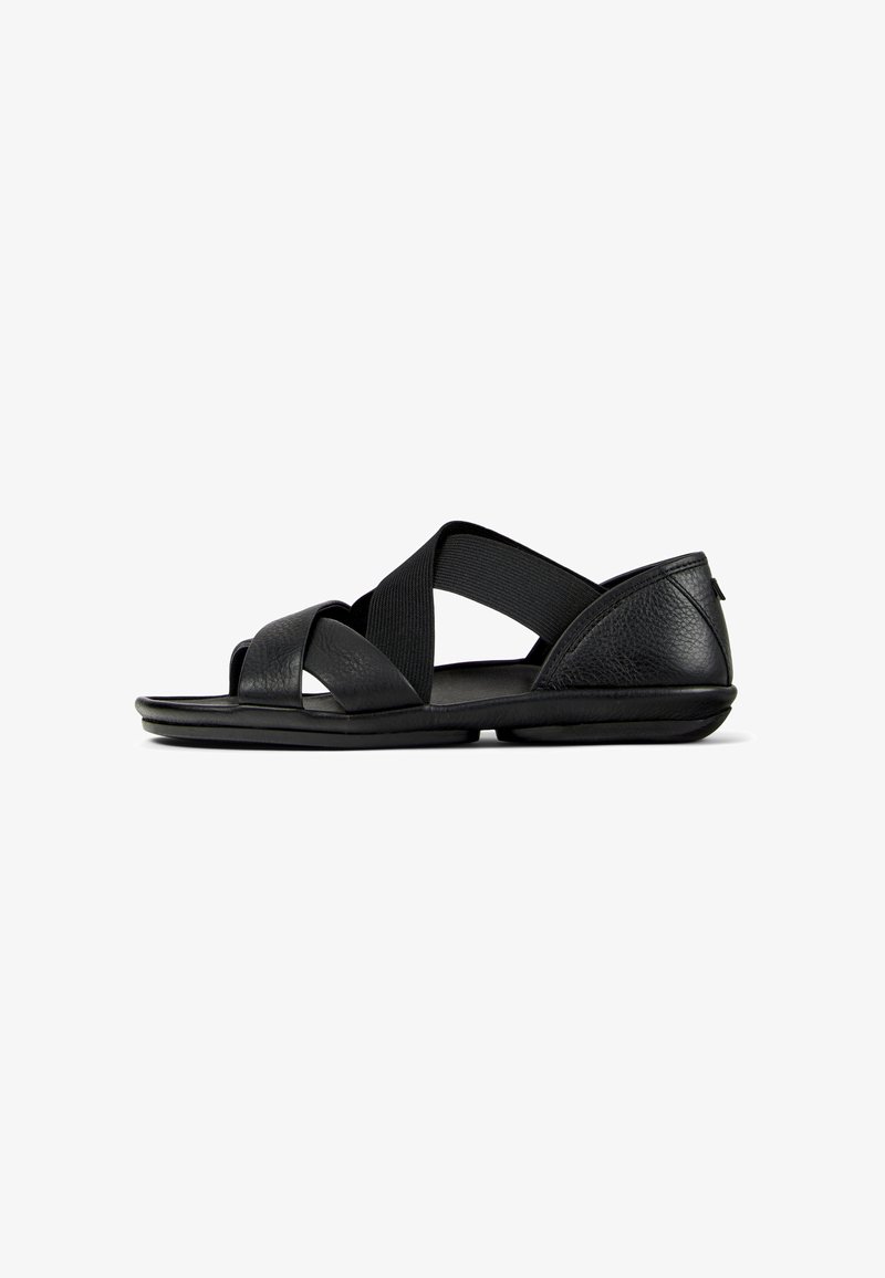 Sort sandal med åben tå med krydsede elastiske stropper, tekstureret hælstøtte og flad polstret sål, vist i sideprofil på hvid baggrund.