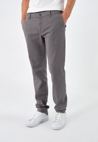 Chinos gris à coupe slim, dotés d'une fermeture à bouton, passants pour ceinture, poches latérales et d'une texture en coton lisse, associés à des baskets blanches.