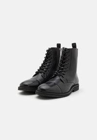 Botas de cuero negro hasta el tobillo con punta redonda, cordones en la parte delantera y cremallera lateral. Superficie texturizada y suela de goma resistente.