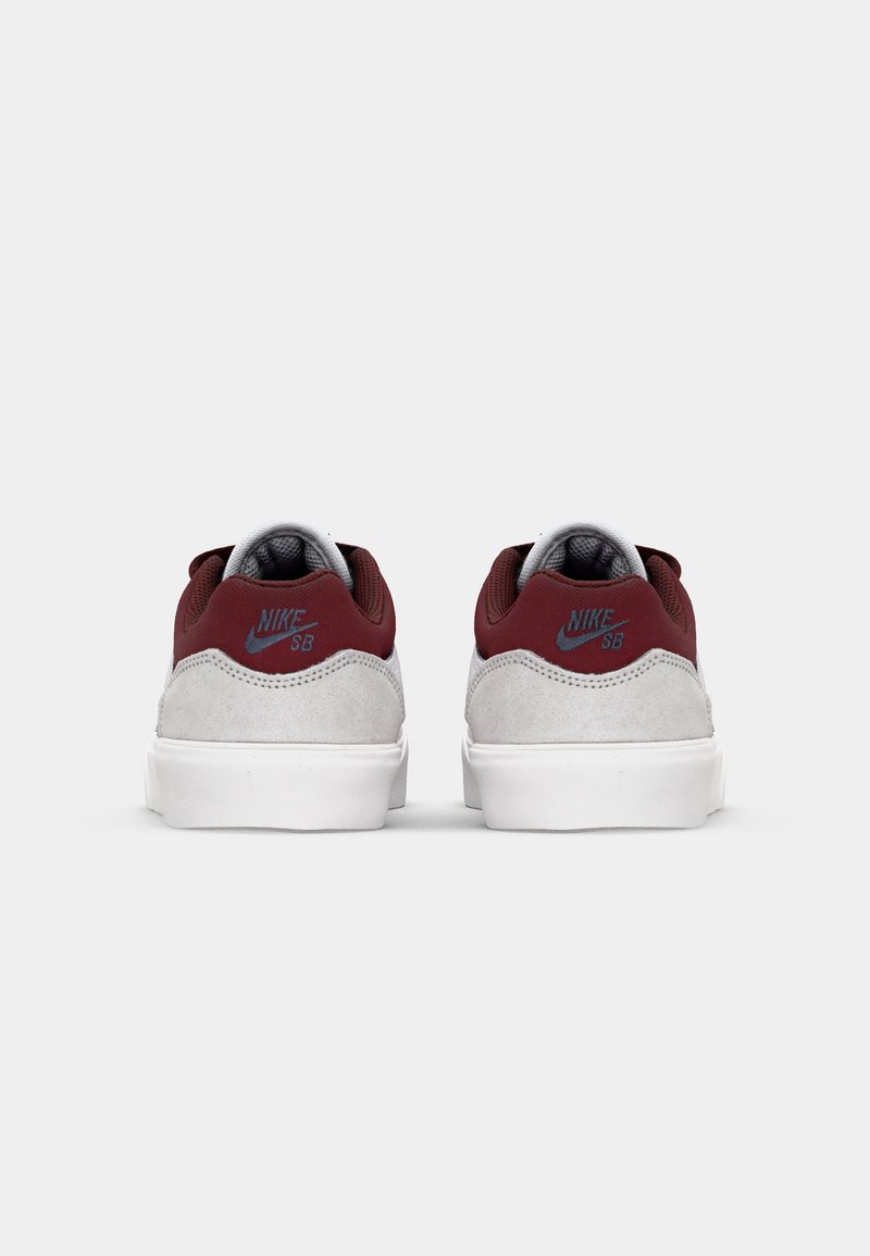 Chaussures Nike SB avec un upper en suède gris et des accents en tissu bordeaux. Elles présentent une semelle blanche et un doublure grise, affichant le logo "Nike SB".