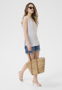 Sac en paille avec des poignées en cuir marron, associé à un haut sans manches à rayures claires et un short en denim, avec des talons blancs à lanières.