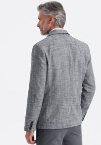 Grå blazer i texturerat tyg, med slag och fyra knappar på ärmarna. Strukturerad passform med en slät yta.