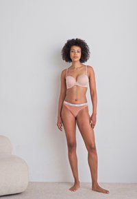 Nude-colored bra and matching panties set, featuring smooth fabric, adjustable straps, and a subtle elastic band around the waist.
