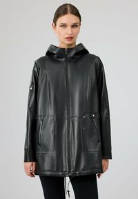 Giacca nera in pelle con cappuccio, chiusura frontale a zip, due grandi tasche anteriori e orlo con cordoncino. Texture liscia e design elegante.