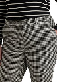 Black and white houndstooth patterned trousers with a tailored fit, featuring side pockets and a smooth textured fabric finish.
