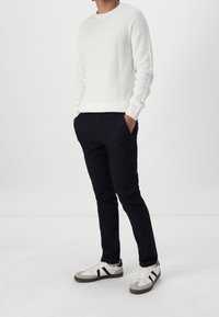 Vitt ribbat tröja, mörka jeans och grå sneakers med svarta accenter. Tröjan har långa ärmar och rund halsringning.