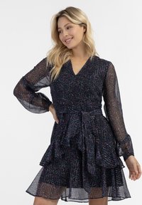 Tumman kukka-kuvioinen mekko, joka on valmistettu läpikuultavasta kankaasta. Mekossa on pitkät puffihihat, V-kaula-aukko, kireä vyötärö ja röyhelöistä kerroksista koostuva hame.