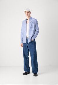 Blue and white striped button-up shirt, denim jeans, and a light-colored cap. The outfit features a relaxed fit and classic design.