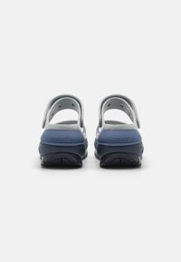 Blå och grå Crocs med öppen baksida, slät textur och ventilationshål. Har varumärket på hälen. Lätt design.