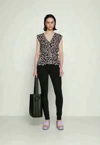 Blusa com padrão floral em tons escuros, com mangas volumosas, combinada com jeans pretos justos, sapatos de plataforma em lavanda e uma bolsa tote preta.