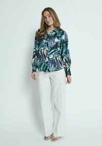 Blusa de manga larga con estampado de hojas tropicales en tonos verde azulado, negro y crema, combinada con pantalones anchos blancos y sandalias planas.