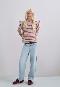 Suéter a rayas beige con hombros con volantes, combinado con pantalones de mezclilla de pierna ancha de color azul claro. Zapatos burdeos y un cinturón marrón completan el conjunto.