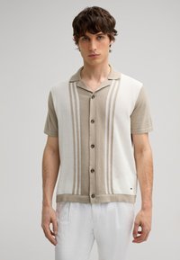 Short-sleeve shirt with a beige and white color block design, featuring vertical stripes and black buttons, made from a textured fabric.