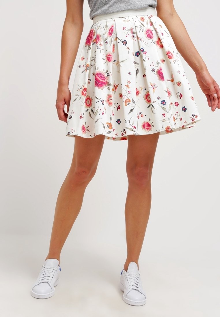 Blumenmusterrock mit weißem Hintergrund, plissiertem Design und lebhaften pinken und blauen Akzenten. Kombiniert mit weißen Sneakers.